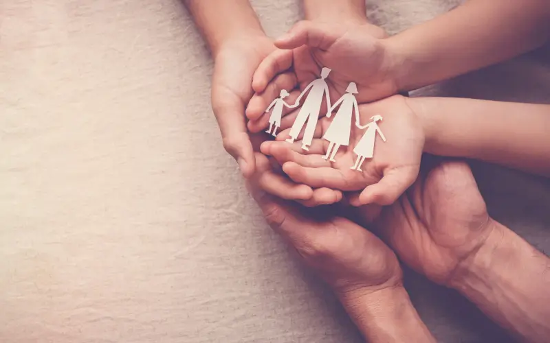 6 mains tiennent une figurine en papier représentant une famille